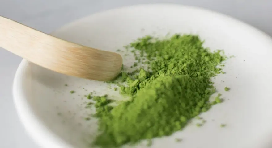 Zielony proszek matcha na białej miseczce, gotowy do przygotowania napoju. Poznaj, jak smakuje matcha – intensywnie, lekko gorzko, z nutą słodyczy.