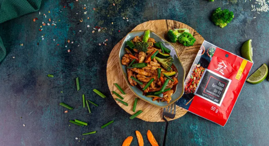 Aksamitny kurczak po kantońsku z brokułami i marchewką, gotowy do podania. Obok paczka pasty do stir-fry.