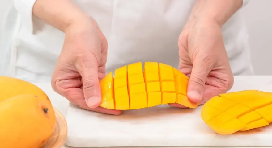 Ręce trzymają pokrojonego w kostkę mango. Ten soczysty owoc jest gotowy do jedzenia.