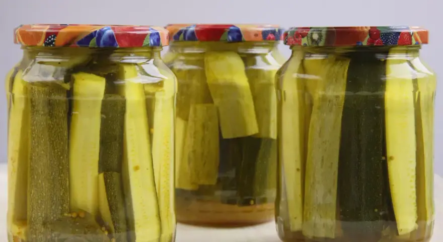Słoiki z cukinią w zalewie słodko-kwaśnej z curry. Zioła i przyprawy dodają smaku.