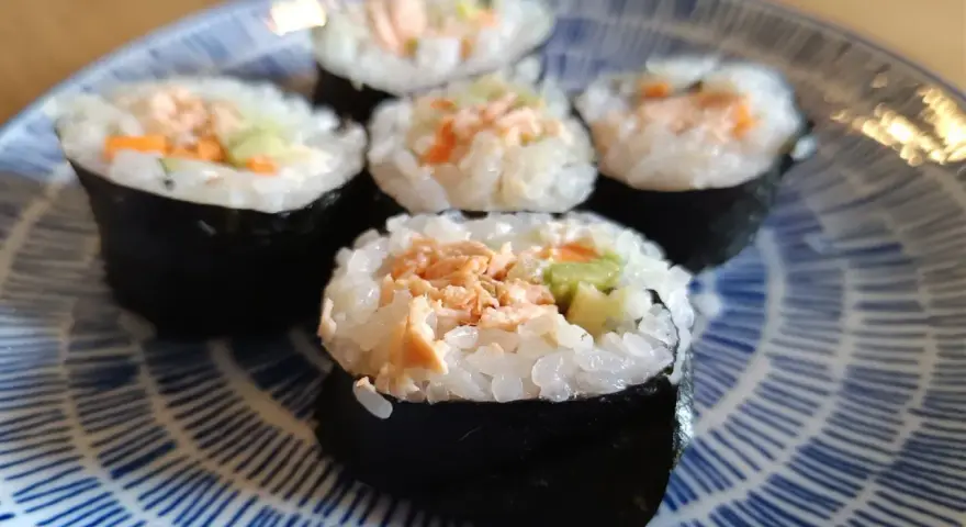 Pięć kawałków sushi z łososiem, ryżem i warzywami na niebiesko-białym talerzu.