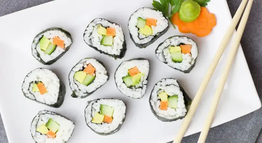 Smaczne futomaki z awokado, ogórkiem i marchewką, udekorowane natką pietruszki i wasabi.