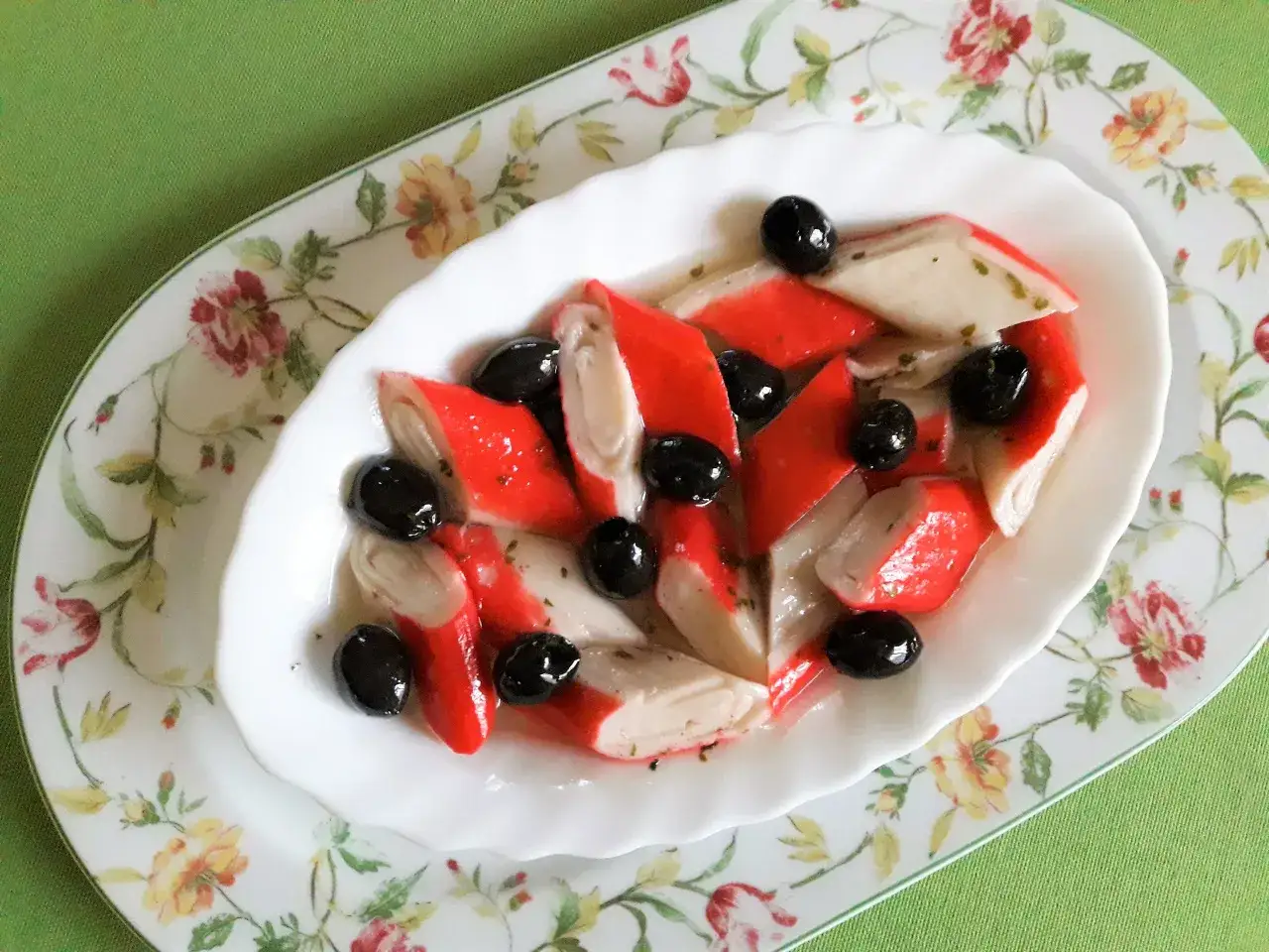 Pyszne paluszki surimi z czarnymi oliwkami w sosie, podane na ozdobnym talerzu.