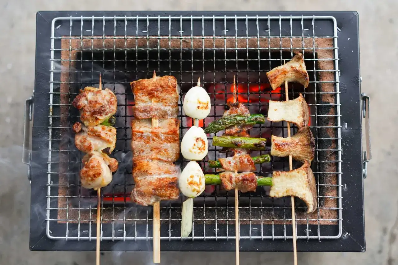 Pyszne yakitori z kurczakiem, boczkiem, jajkami przepiórczymi, szparagami i grzybami na grillu.
