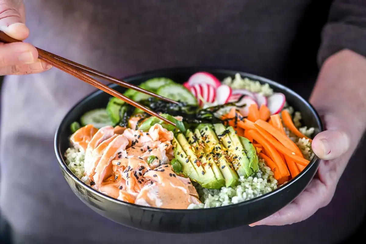 Miseczka poke bowl z łososiem, awokado, ogórkiem, marchewką i rzodkiewką, polana sosem. Idealna zaprawa do sushi.