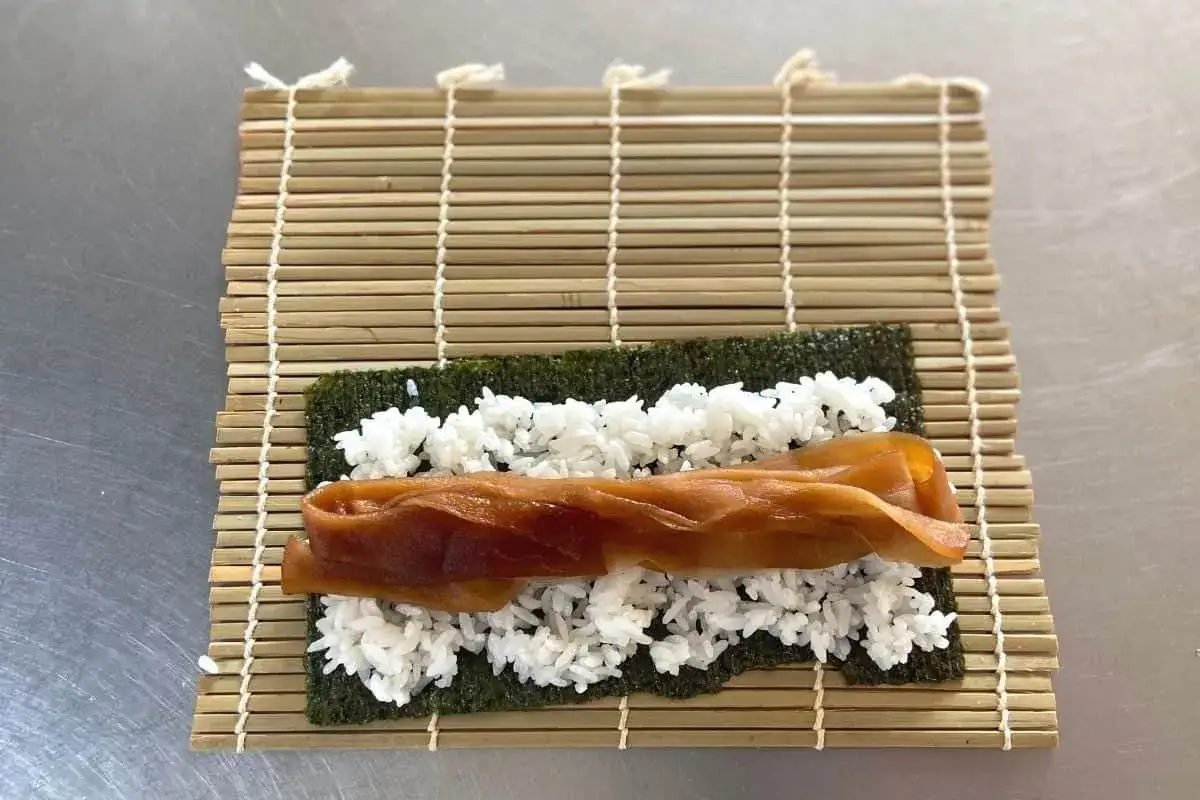 Sushi nori z ryżem i kandyzowaną tykwą na bambusowej macie.
