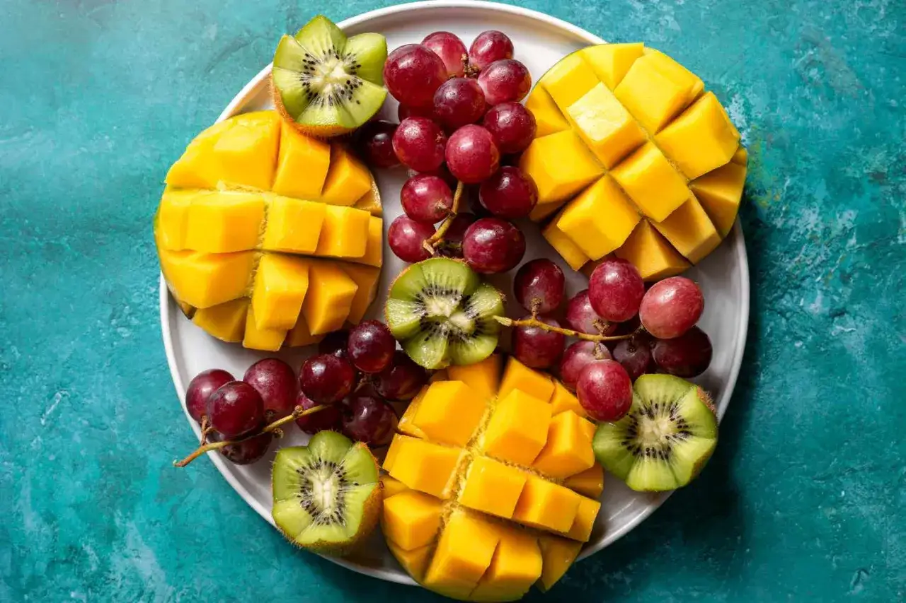 Talerz z pokrojonym mango, kiwi i winogronami. Jak jeść mango? Wystarczy pokroić w kostkę i wyjadać łyżeczką.